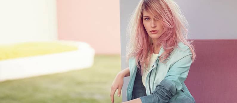 Model with long blonde hair with a pink wash sitting on a bench outside.